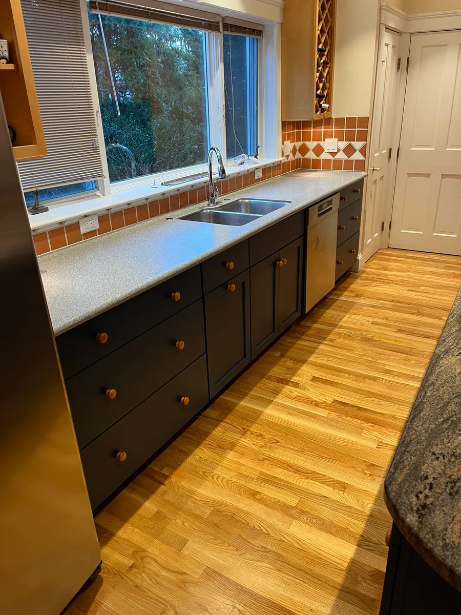 A renovated kitchen with dark lower cabinets, a stainless sink and wood floors